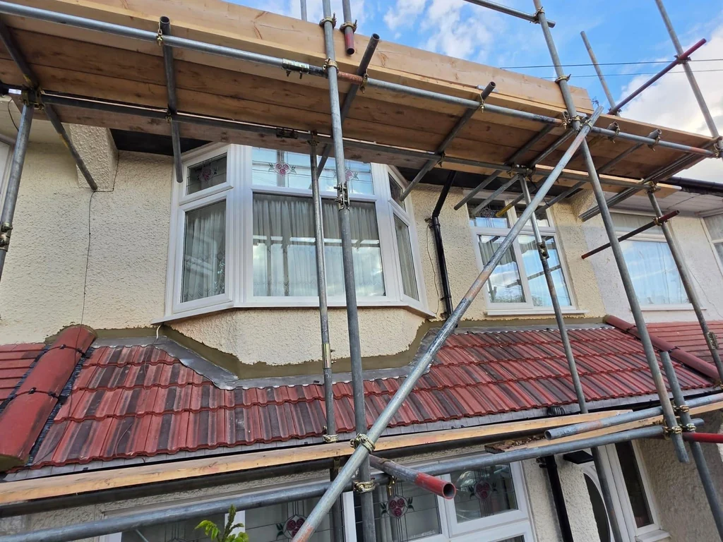 Red tiled bay roof beneath scaffold on a rendered house