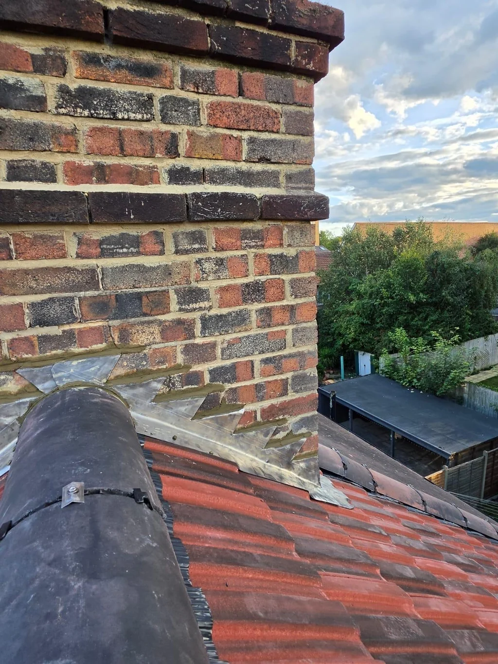 Brick chimney with lead flashing beside a dark ridge and red tiles