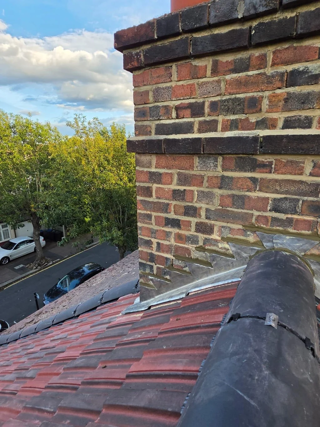 Brick chimney and lead flashing above red roof tiles