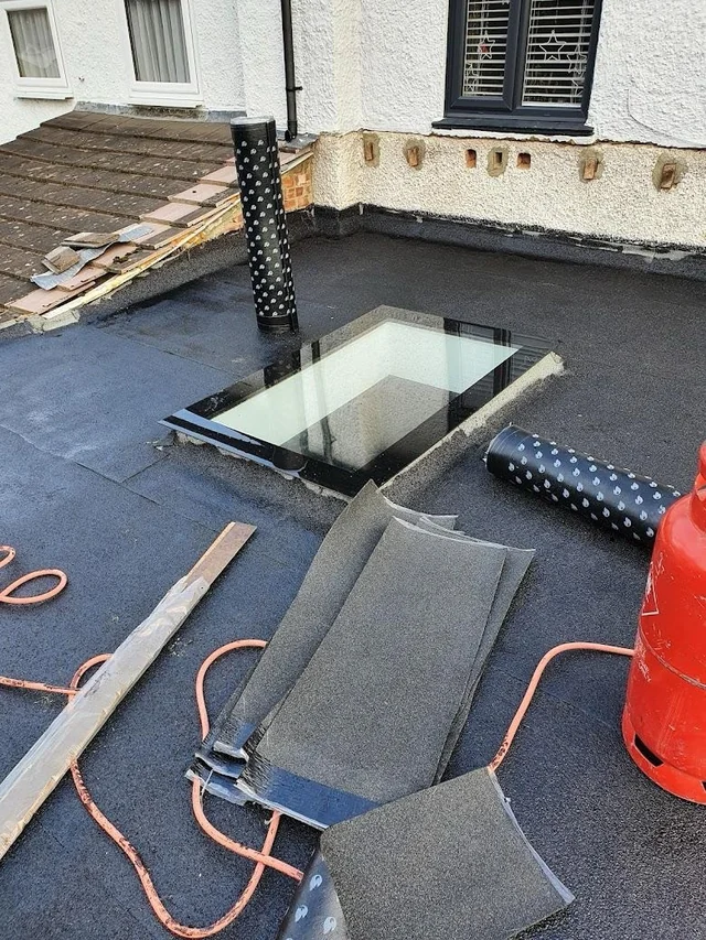 Felt rolls and tools beside a rooflight on a flat roof