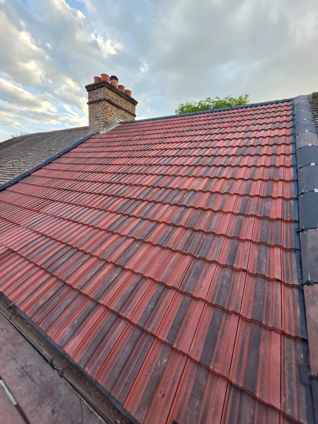 Red tiled roof slope and brick chimney beneath cloudy sky