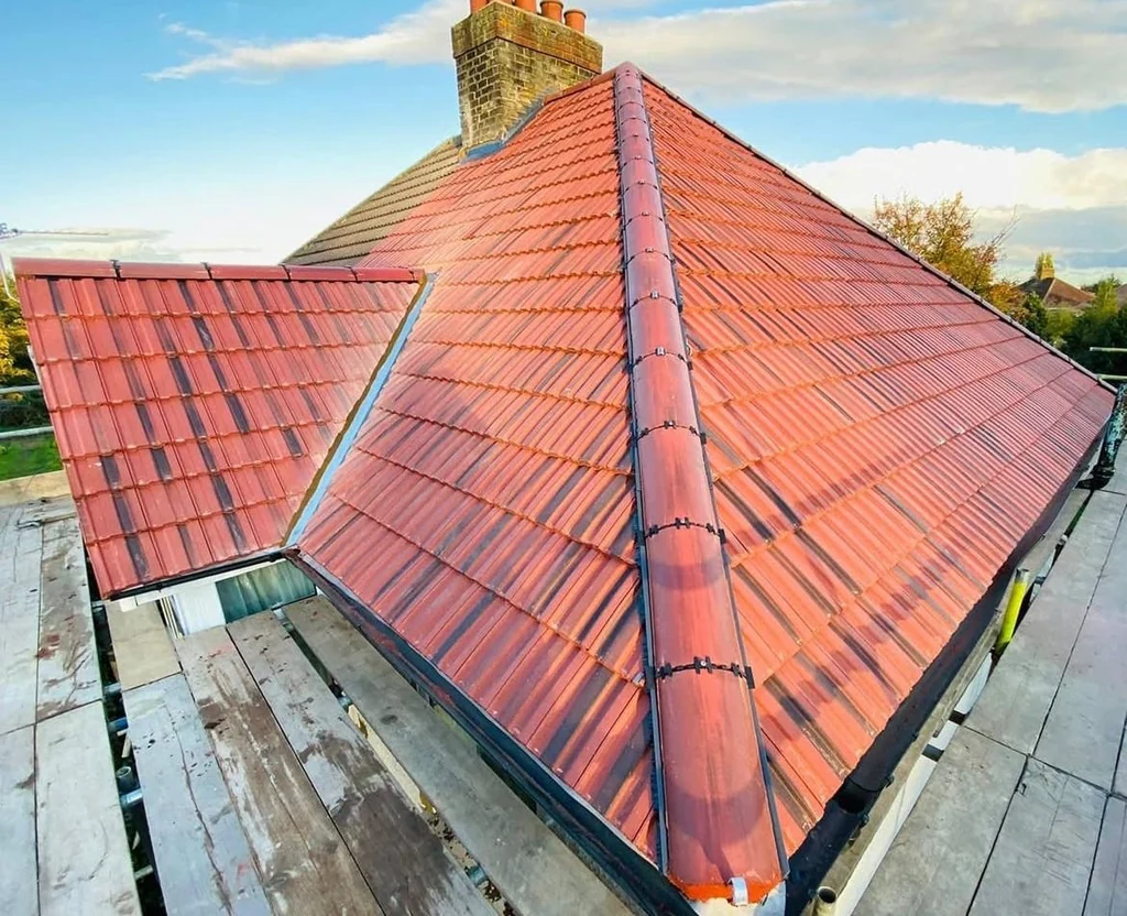 Red tiled hip roof with a chimney and scaffold under blue sky