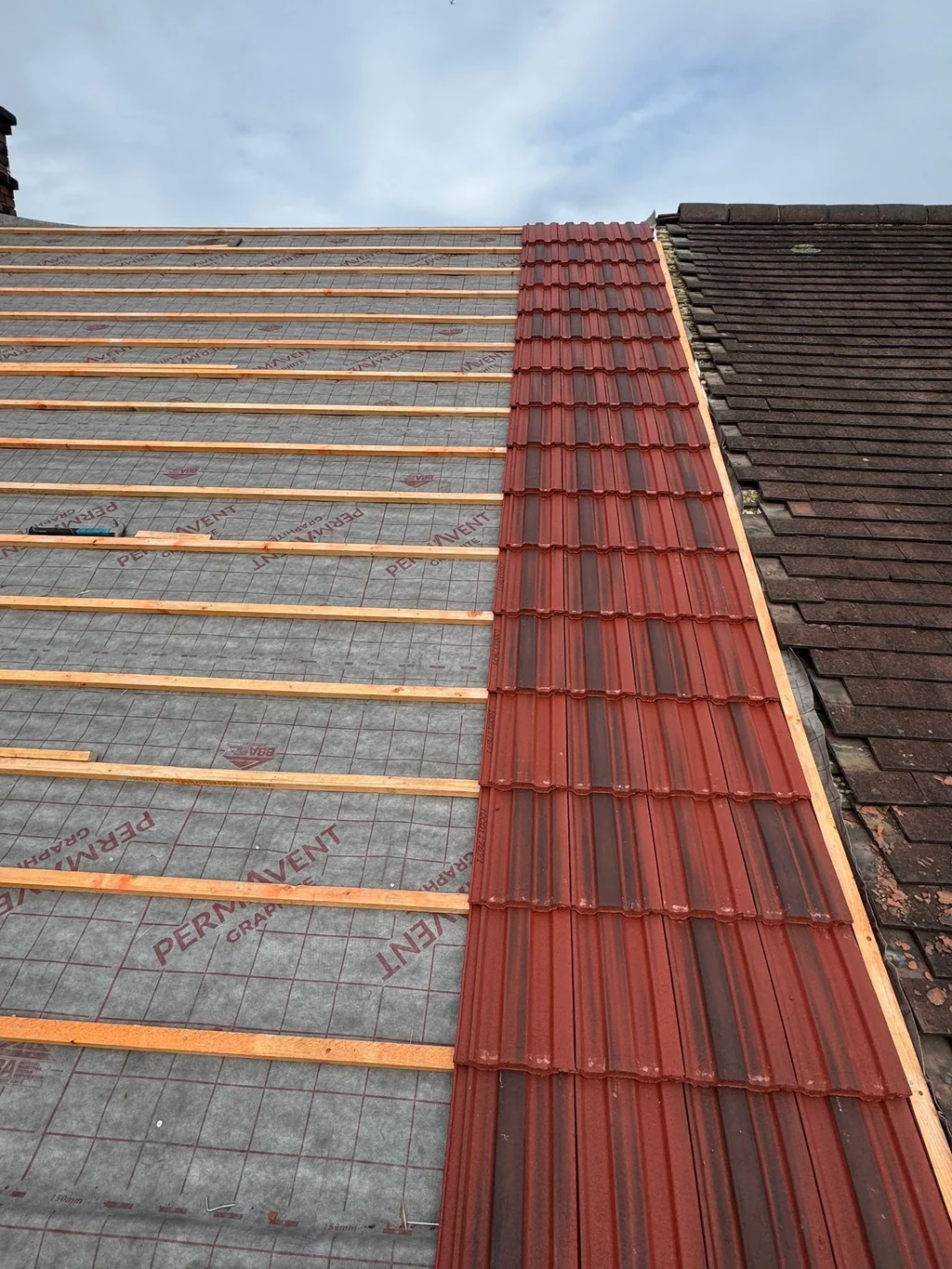 Red tiles being laid beside exposed roof battens