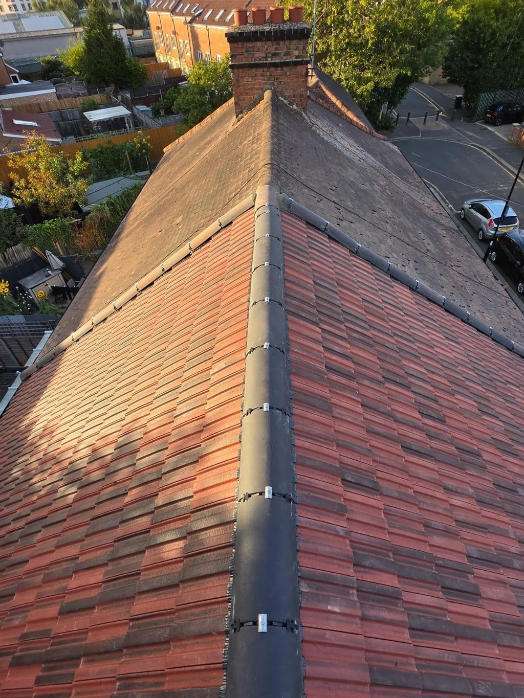Dark ridge between red tiled roof slopes leading to a chimney