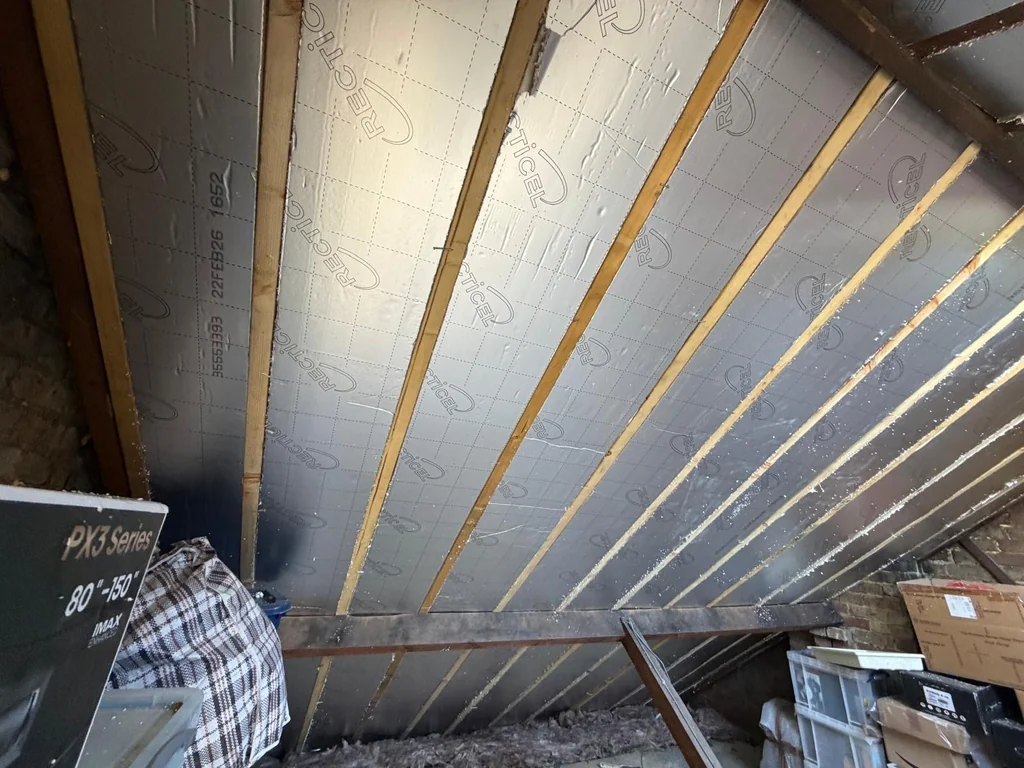 Foil-faced insulation boards between timber rafters in a loft