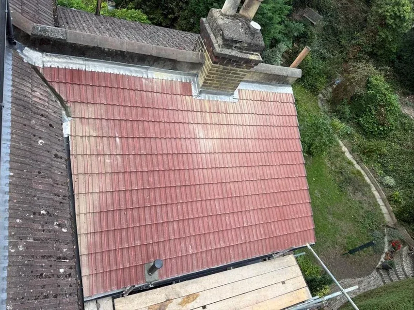 Weathered red tiles on a roof slope beside a chimney