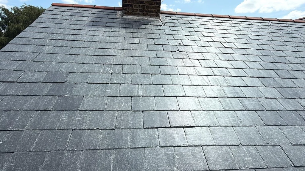 Close grey slate roof courses beneath a brick chimney