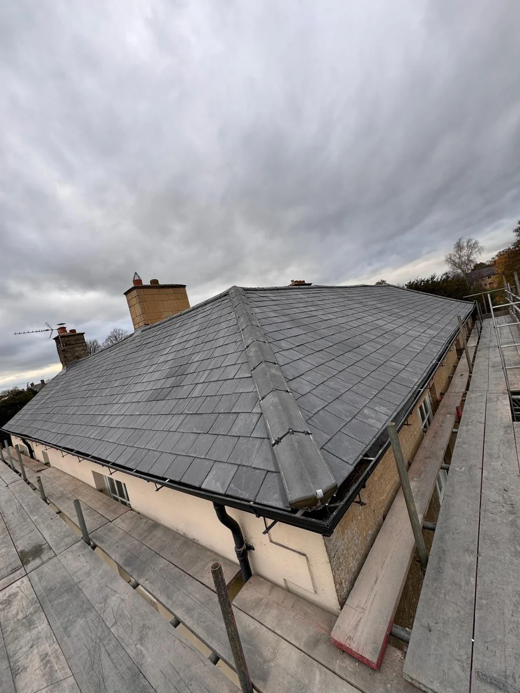 Grey slate-style hip roof above a rendered bungalow and scaffold